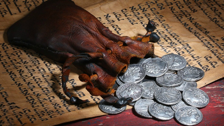 The 30 pieces of silver that Judas betrayed Jesus with spilling out of an old leather money bag on top of a Hebrew manuscript.